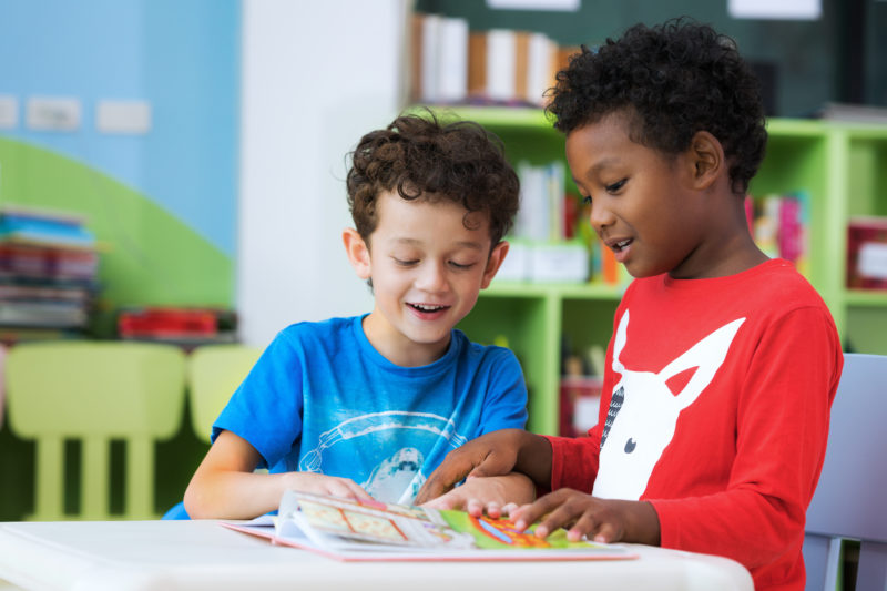 Two boys looking at a book together in class.