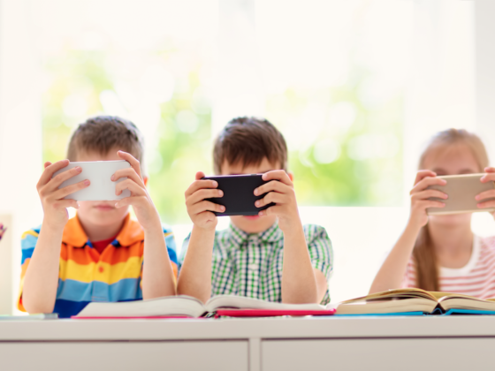 Elementary students surrounded by books reading on smartphones