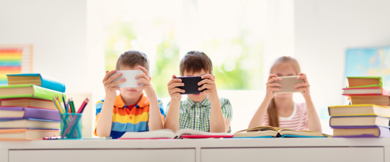 Elementary students surrounded by books reading on smartphones