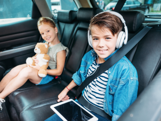 Kids in the car with a boy wearing headphones and using a tablet.