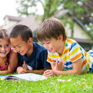 Three children reading a book together outdoors, representing fun summer reading activities for kids with Epic Books for Kids.