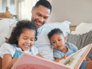 Everyone gets a turn to read. Shot of a young man reading to his kids on the sofa at home.