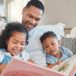 Everyone gets a turn to read. Shot of a young man reading to his kids on the sofa at home.